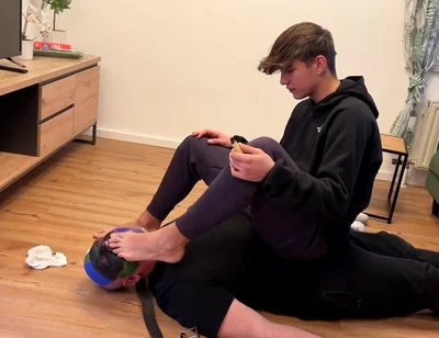 German master sitting on feet licking boy